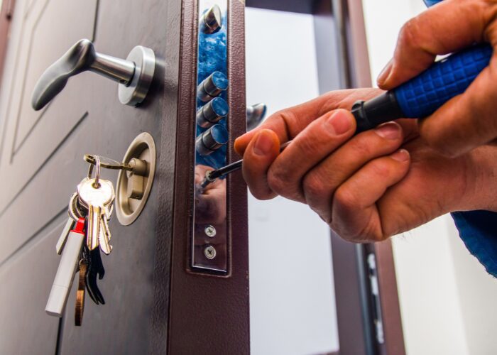 Individual repairing a door lock with a screwdriver, next to a sign for emergency locksmith assistance.